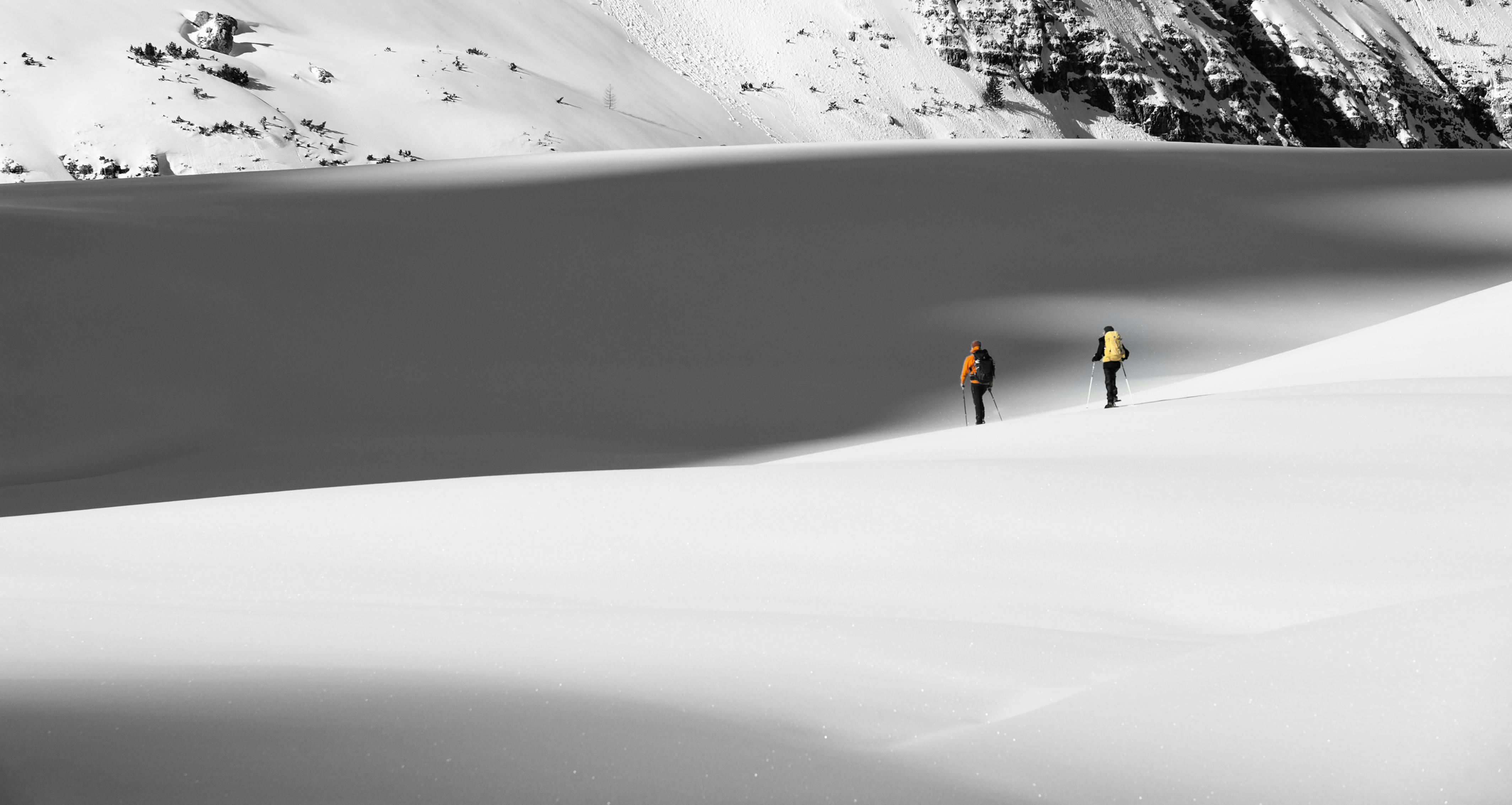 Prescription Goggle Inserts - Two skiers trekking across a serene snowy mountain landscape on a bright winter day.