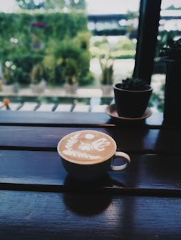 A beautifully crafted cappuccino with latte art on a wooden table, overlooking a garden view.