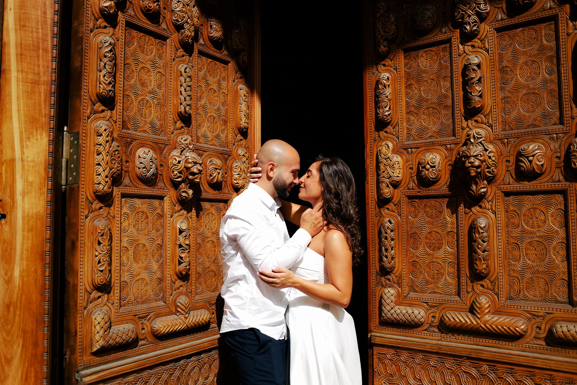 A couple embraces in front of intricately carved wooden doors, capturing a moment of romance.