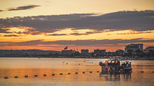 A tranquil sunset scene over the water with a boat in Istanbul, Turkey, capturing the city's skyline and warm hues.