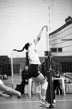 Black and white image of a woman playing volleyball, capturing dynamic mid-air action.