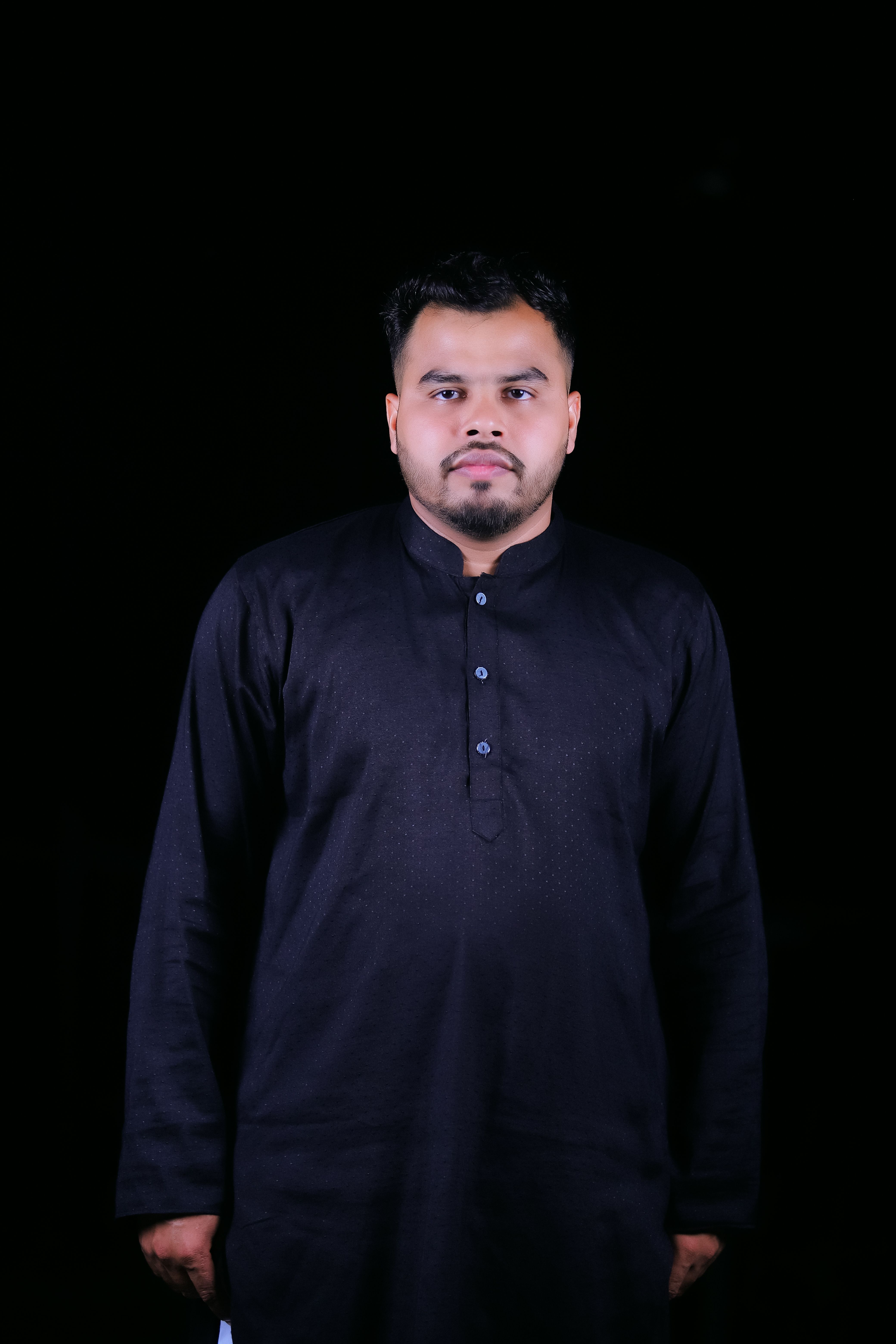 Man in black traditional outfit posing against a dark background.