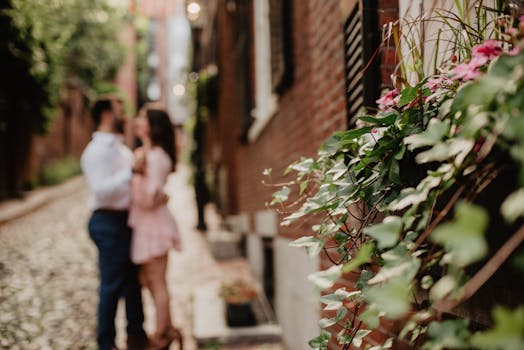 Blurred couple embracing in Boston alley, with vibrant greenery and intimacy captured.