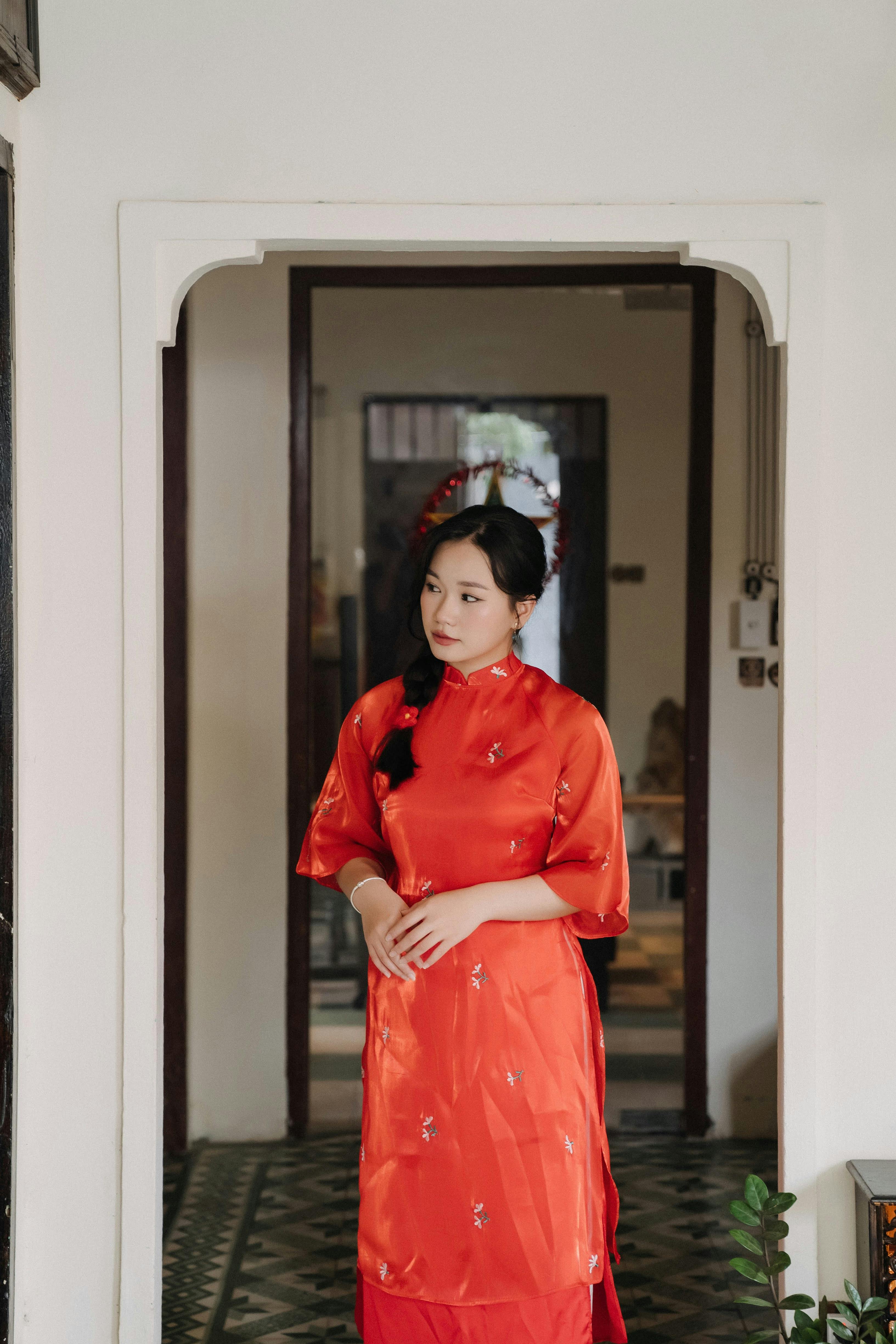 A woman wearing a traditional red dress stands elegantly in a serene indoor corridor.