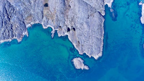 Free Stunning aerial shot of a rocky coastline merging into vibrant blue waters. Stock Photo