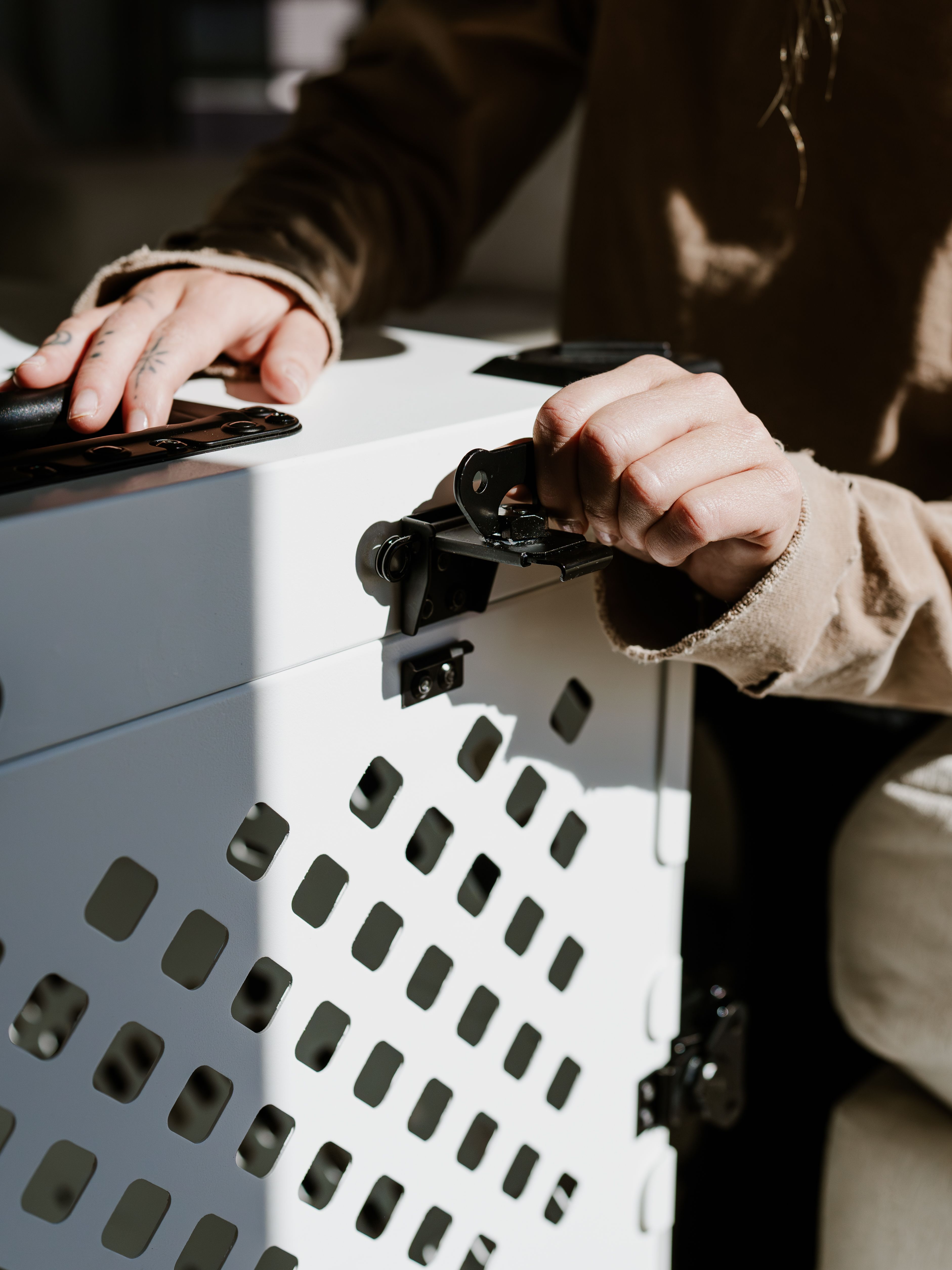Close-up of hands locking a premium pet crate made of high-quality materials indoors.