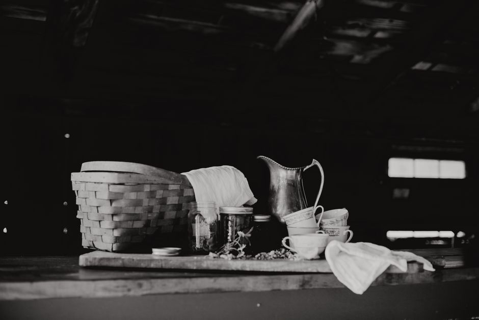 A rustic black and white still life of a tea setting with a basket and utensils.