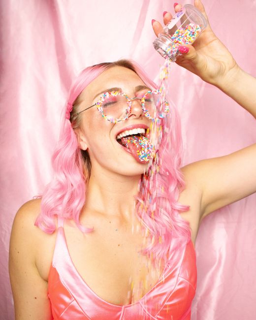 Woman with pink hair and outfit joyfully catching colorful sprinkles, embodying a playful and vibrant style.