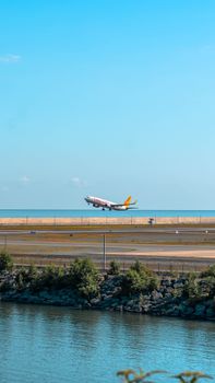 A commercial airplane takes off over a coastal runway with a clear blue sky backdrop.