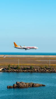 Airliner landing over ocean with clear blue sky at coastal airport during daytime.