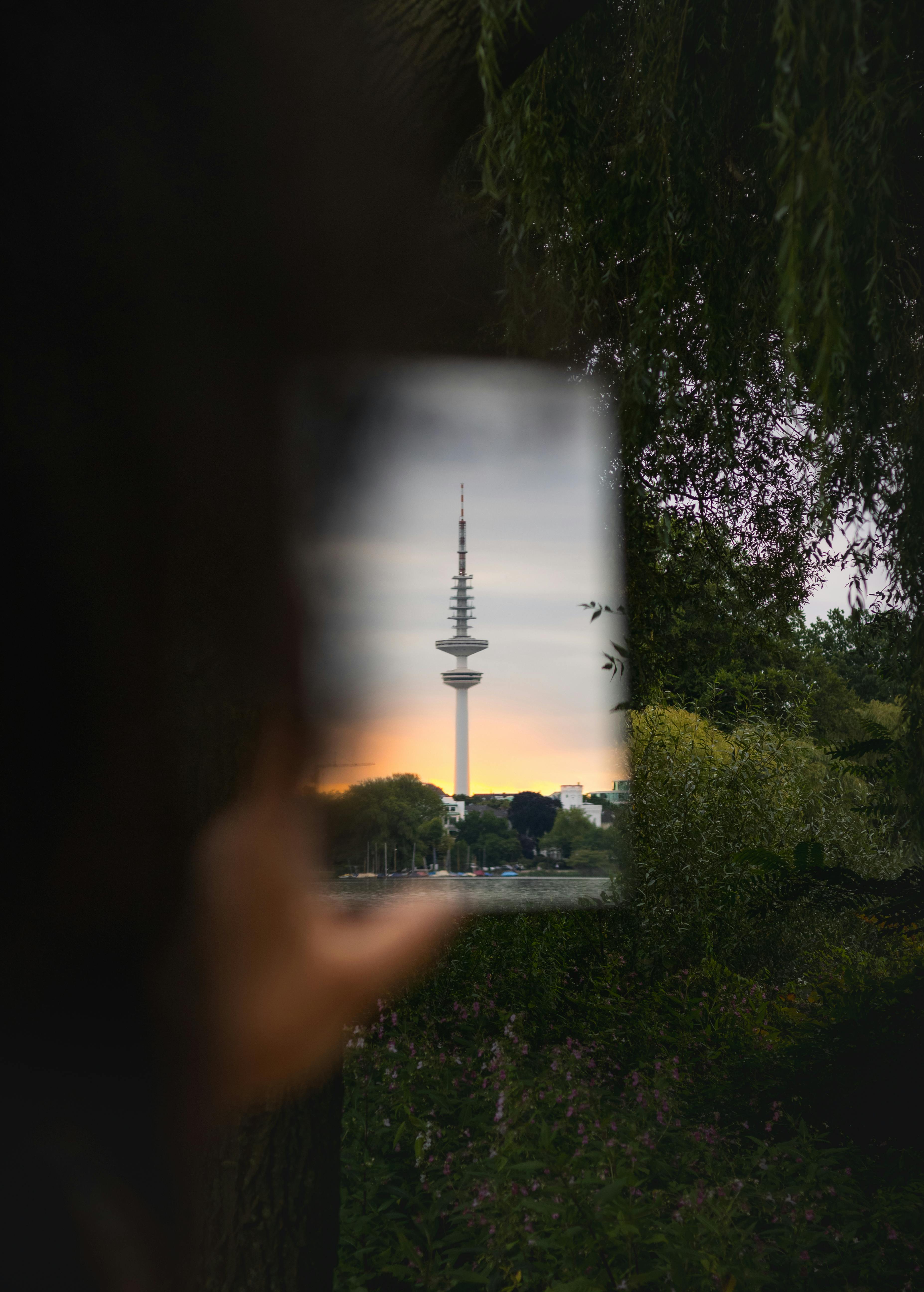 Artistic reflection of Hamburg's television tower in a glass with lush park foreground.