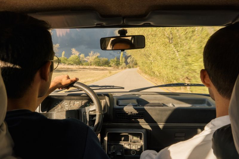 Two adults driving through scenic countryside near Merzifon, Türkiye, in a vintage car.