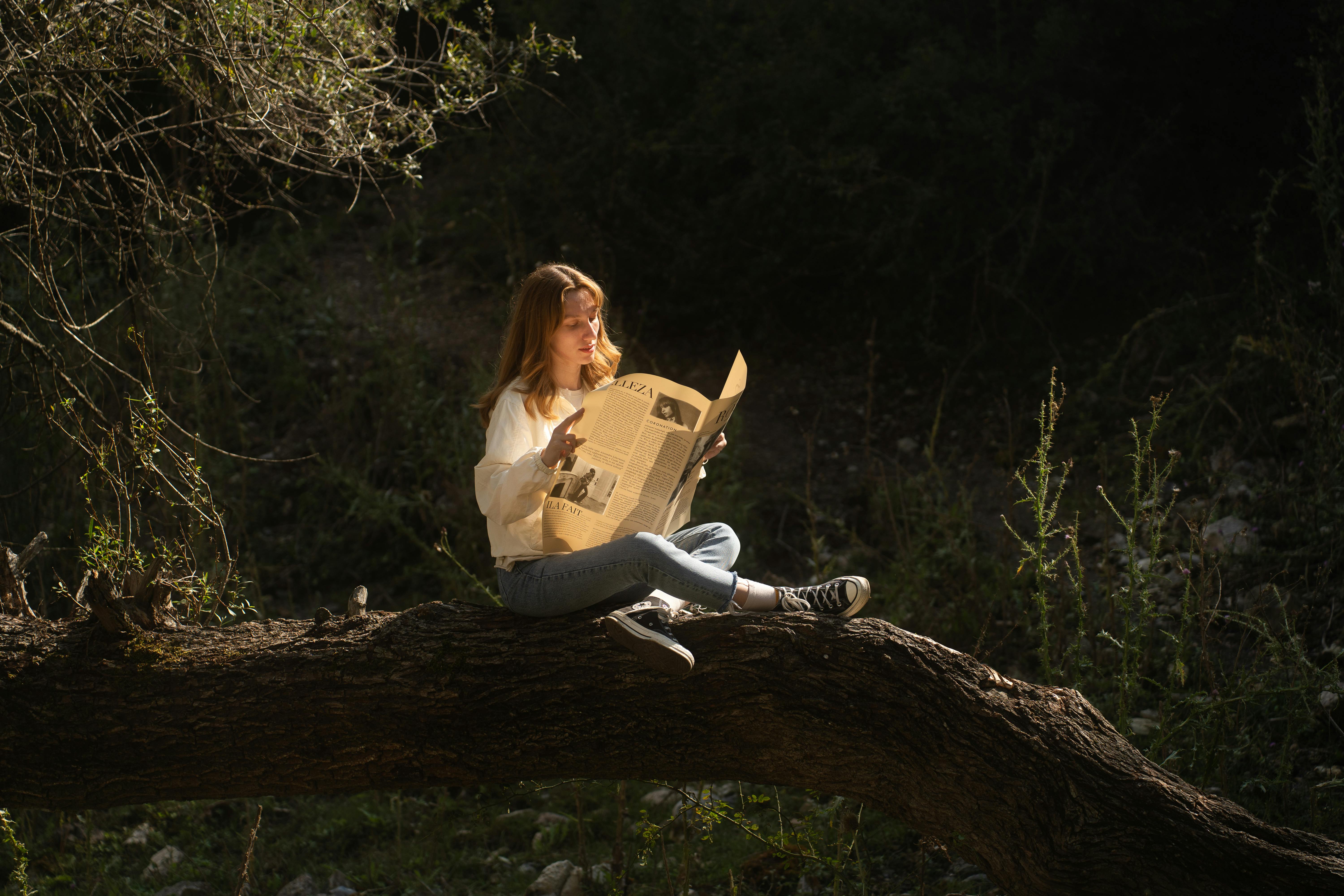 A woman sitting on a tree branch reading a newspaper, illuminated by sunlight, in a forest.