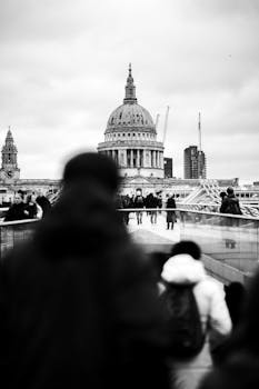 Black and white image of St Paul's Cathedral from Millennium Bridge in London, capturing urban life.