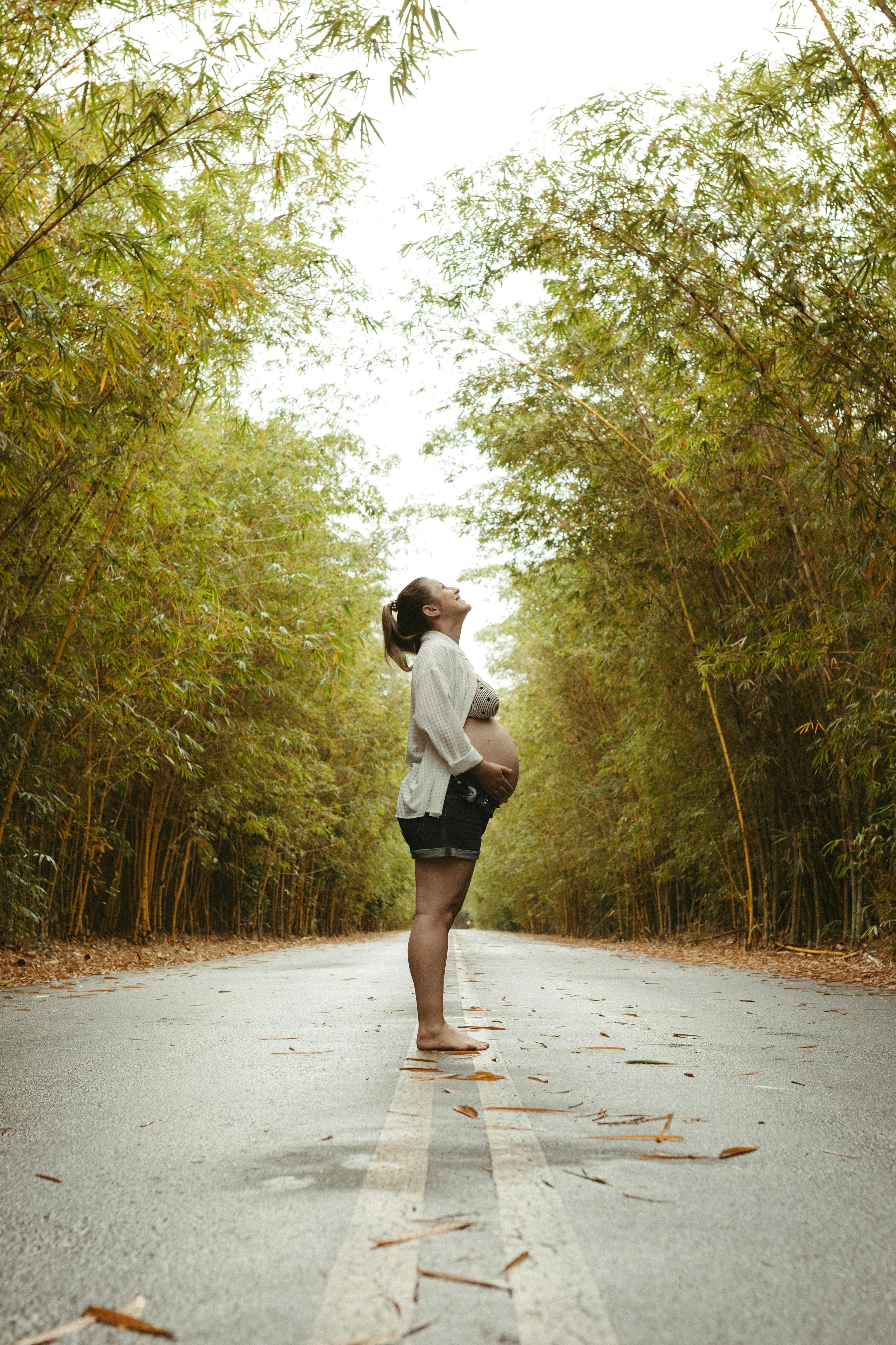 a pregnant woman standing on the road in the middle of a forest