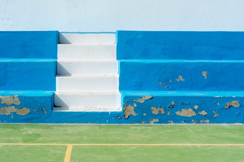 Bright blue and white steps in a sports field with chipped paint and vivid colors.