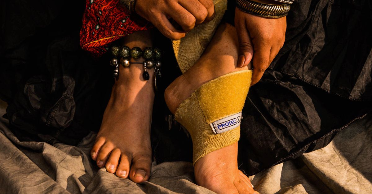Woman adorned in jewelry adjusting foot brace for injury support.