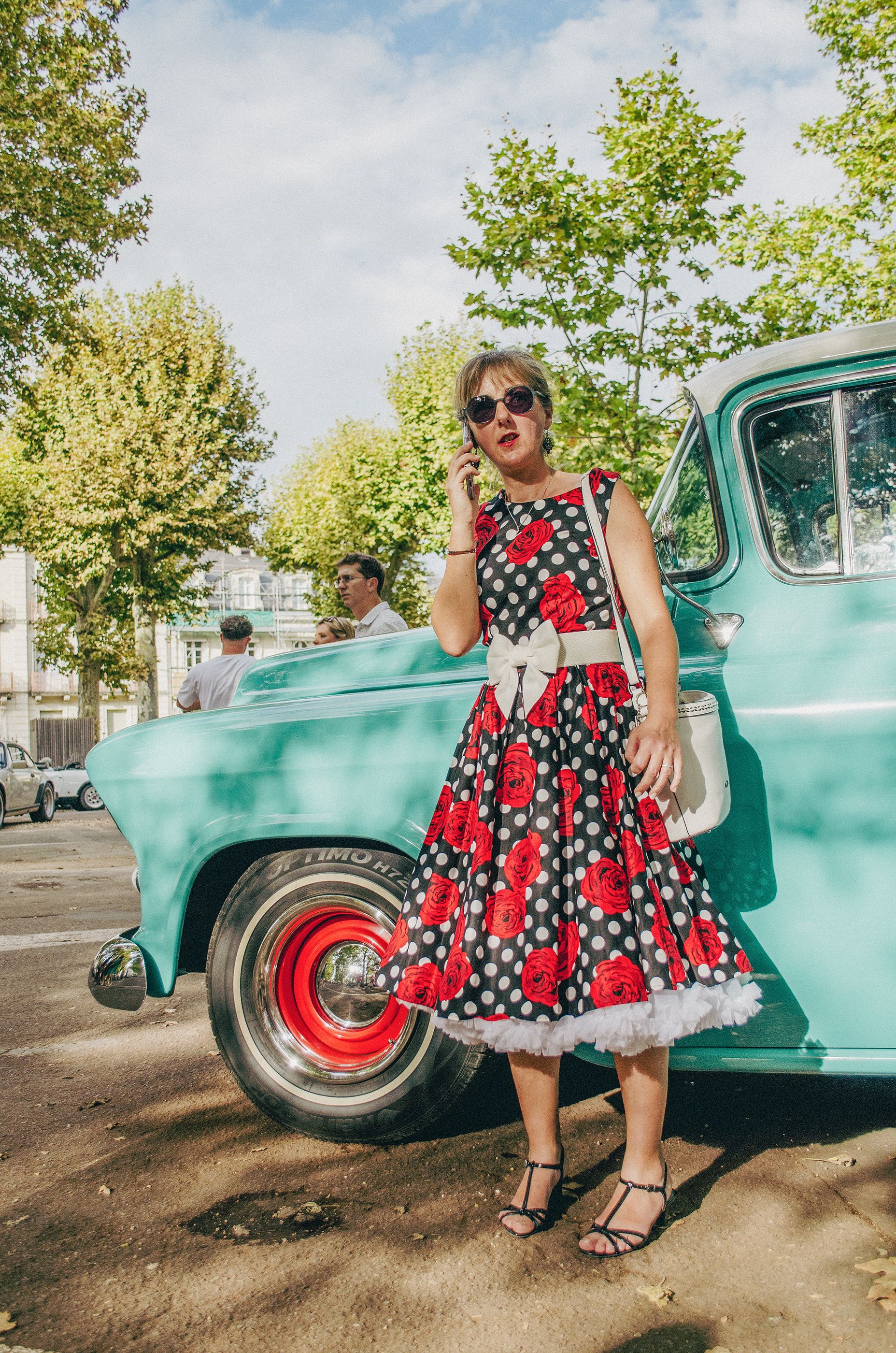Woman in a vintage dress standing by a classic car in Périgueux, France.