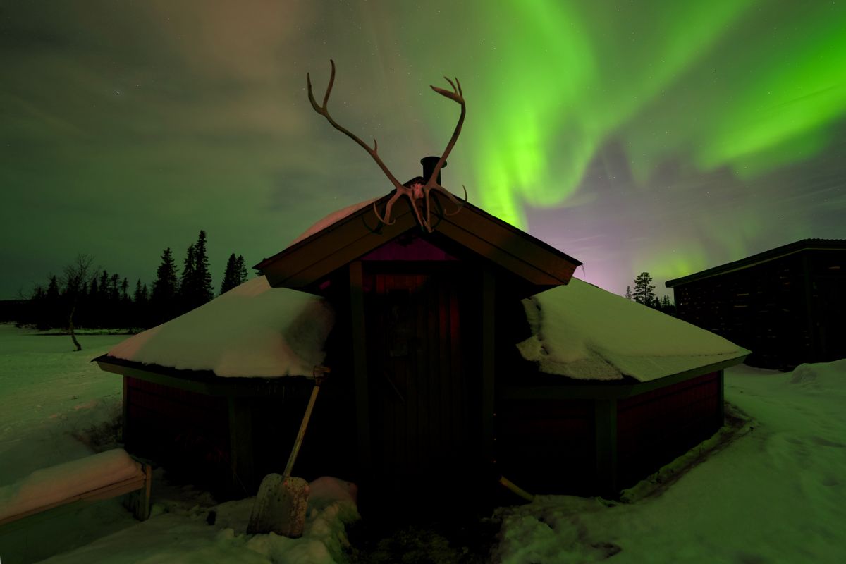 Aurora boreală verde deasupra unei cabane de lemn cu coarne de ren pe acoperiș, în zona Kiruna din nordul Suediei
