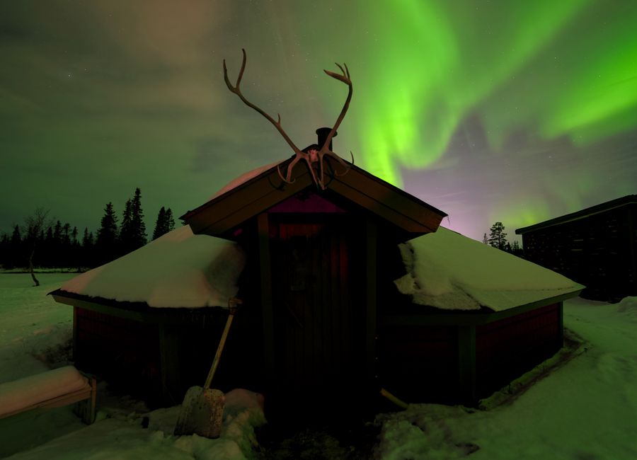 Beautiful Northern Lights over a snowy cabin and forest in Kiruna, Sweden.