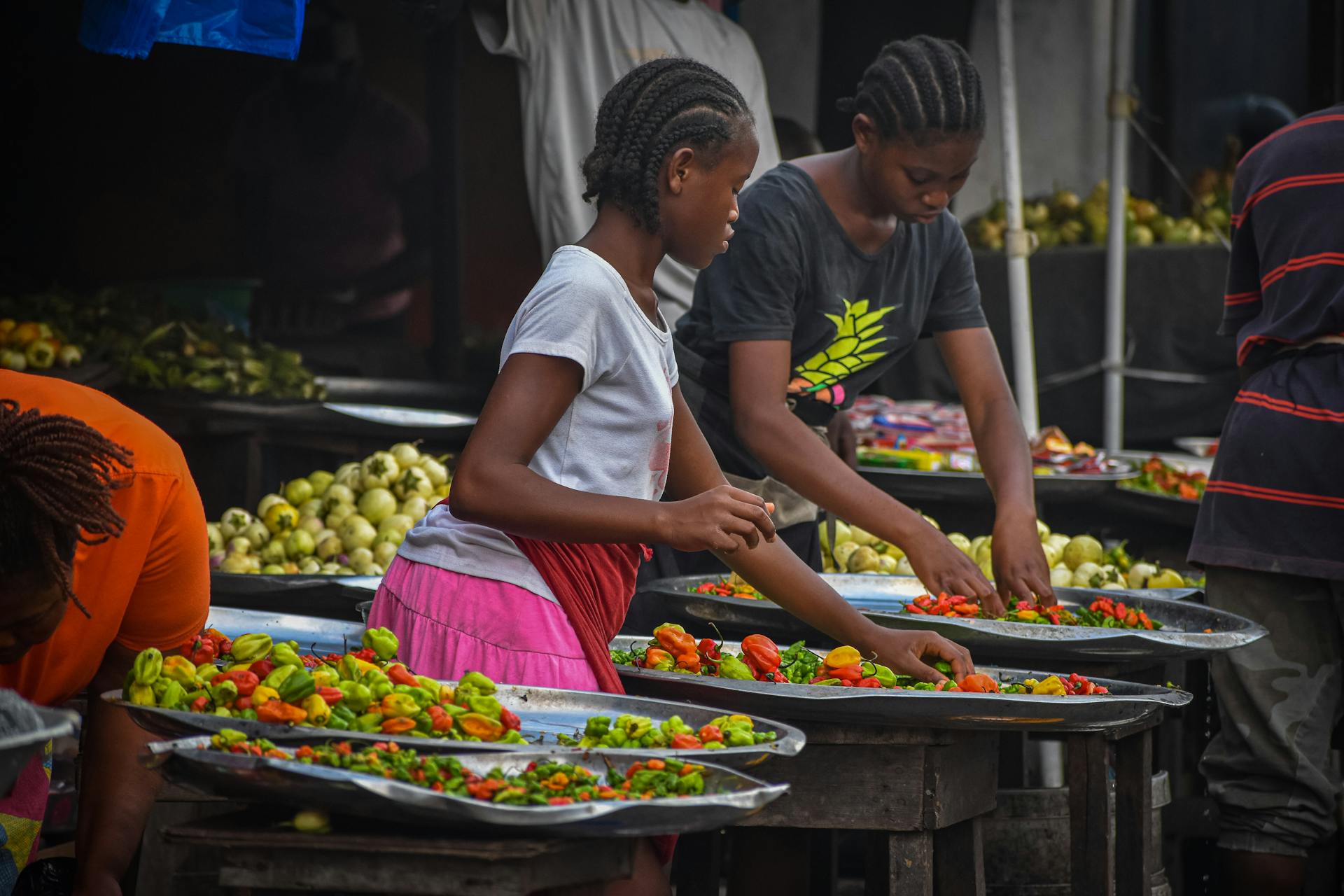 Women sorting vibrant peppers at a bustling Monrovia market.