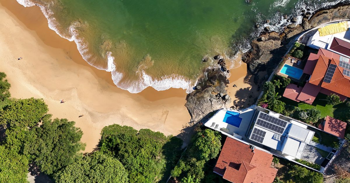 Drone shot of a coastal village with sandy beach and lush greenery. Ideal for travel and real estate insights.