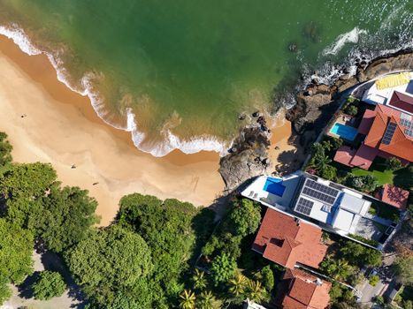 Drone shot of a coastal village with sandy beach and lush greenery. Ideal for travel and real estate insights.