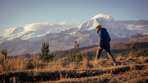 A person hiking through a mountainous region with snow-covered peaks at sunset, offering a serene outdoor experience.