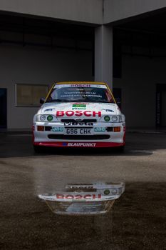 Front view of a rally car reflecting in a puddle, showcasing racing aesthetics.