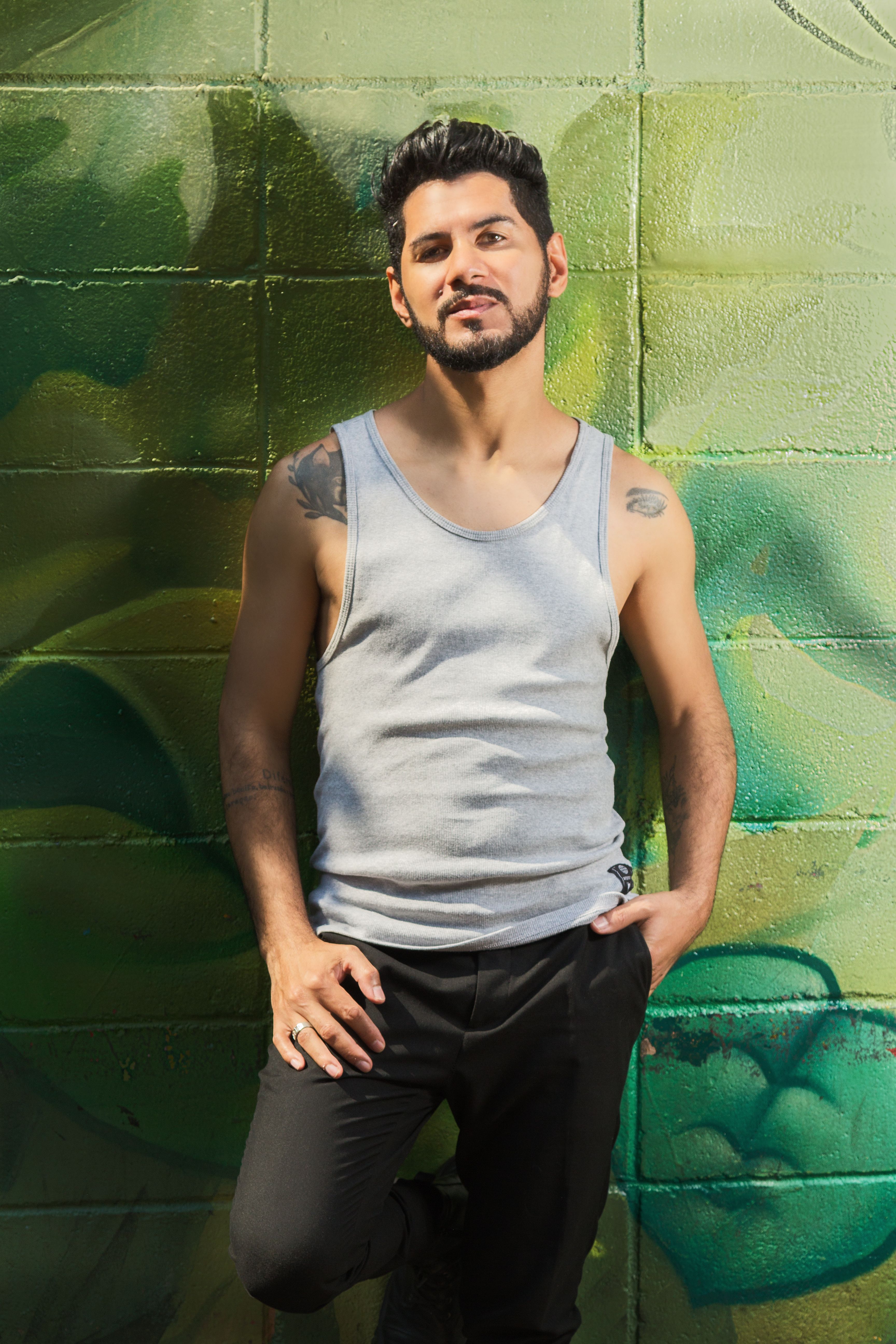 Stylish young man posing against a colorful graffiti wall in the summer sun.