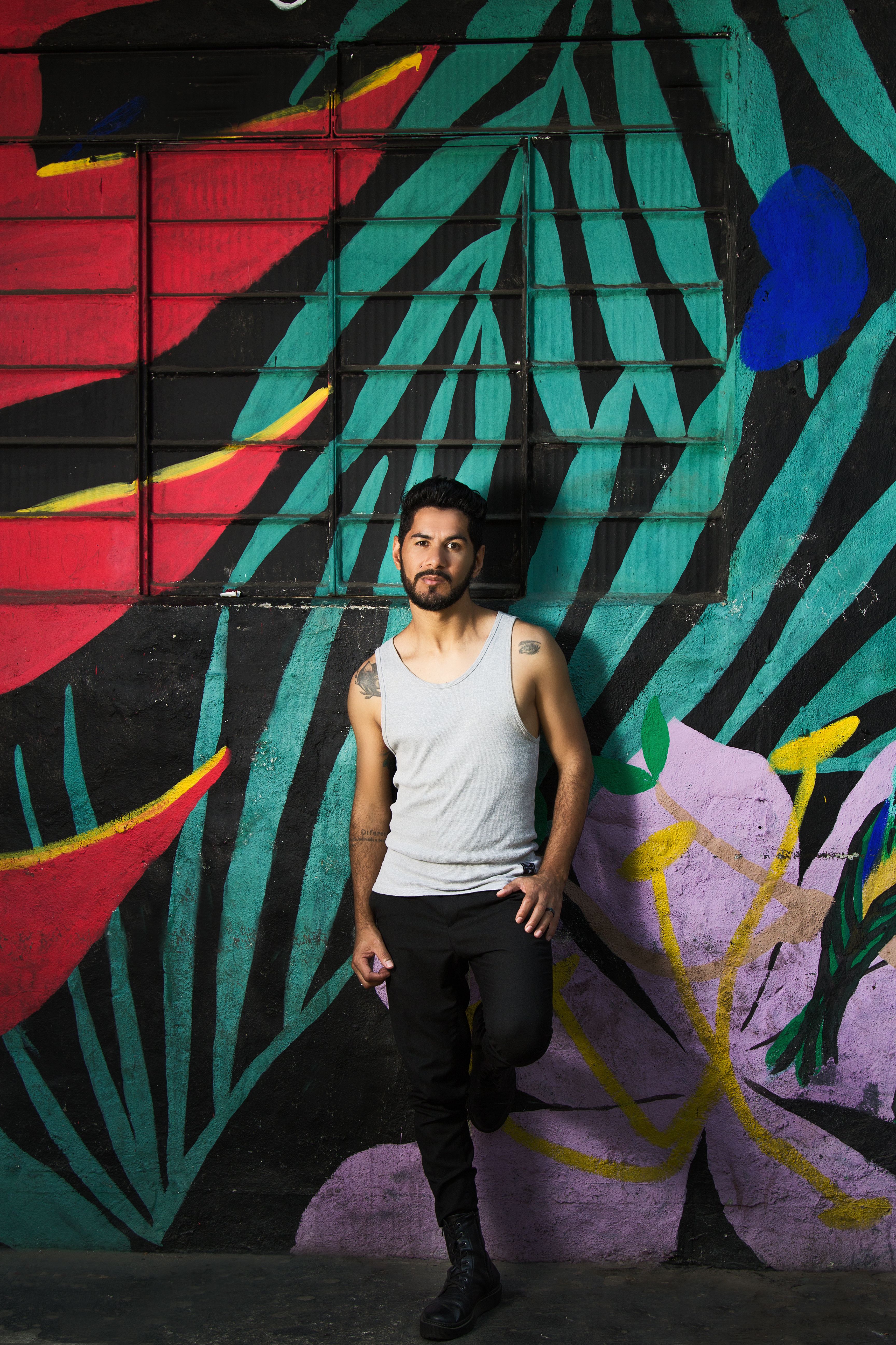 Man standing in front of vibrant street art mural, casual pose and modern style.