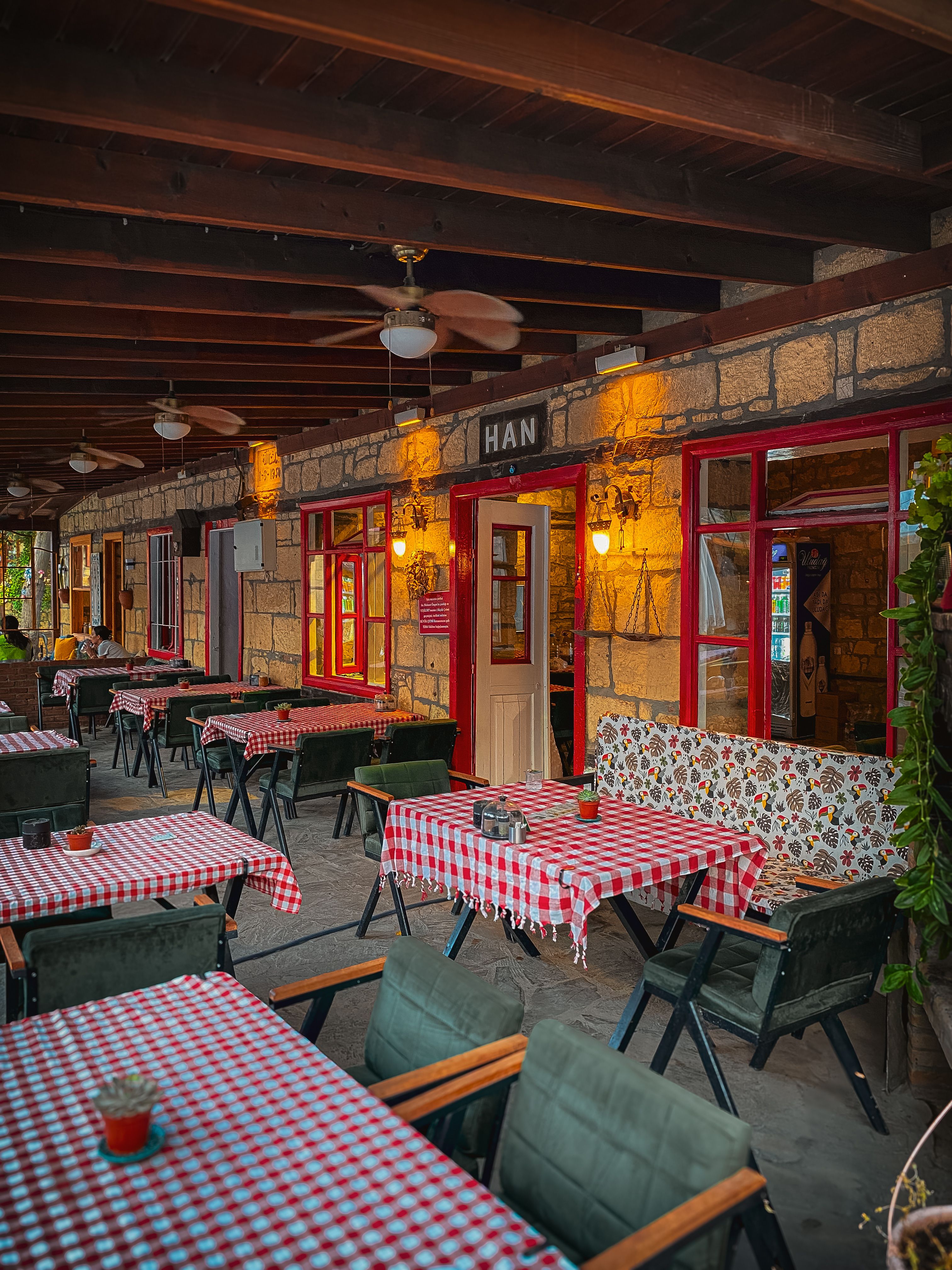 Cozy outdoor café in Çanakkale with red checkered tablecloths and rustic stone walls, ideal for dining al fresco.