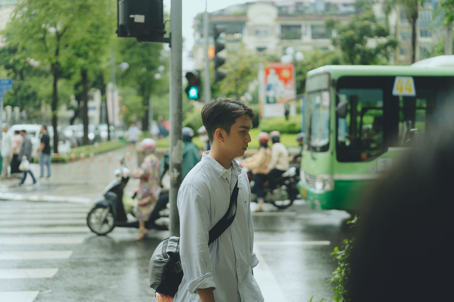 Young man crosses busy street in rainy Ho Chi Minh City, vibrant urban life.