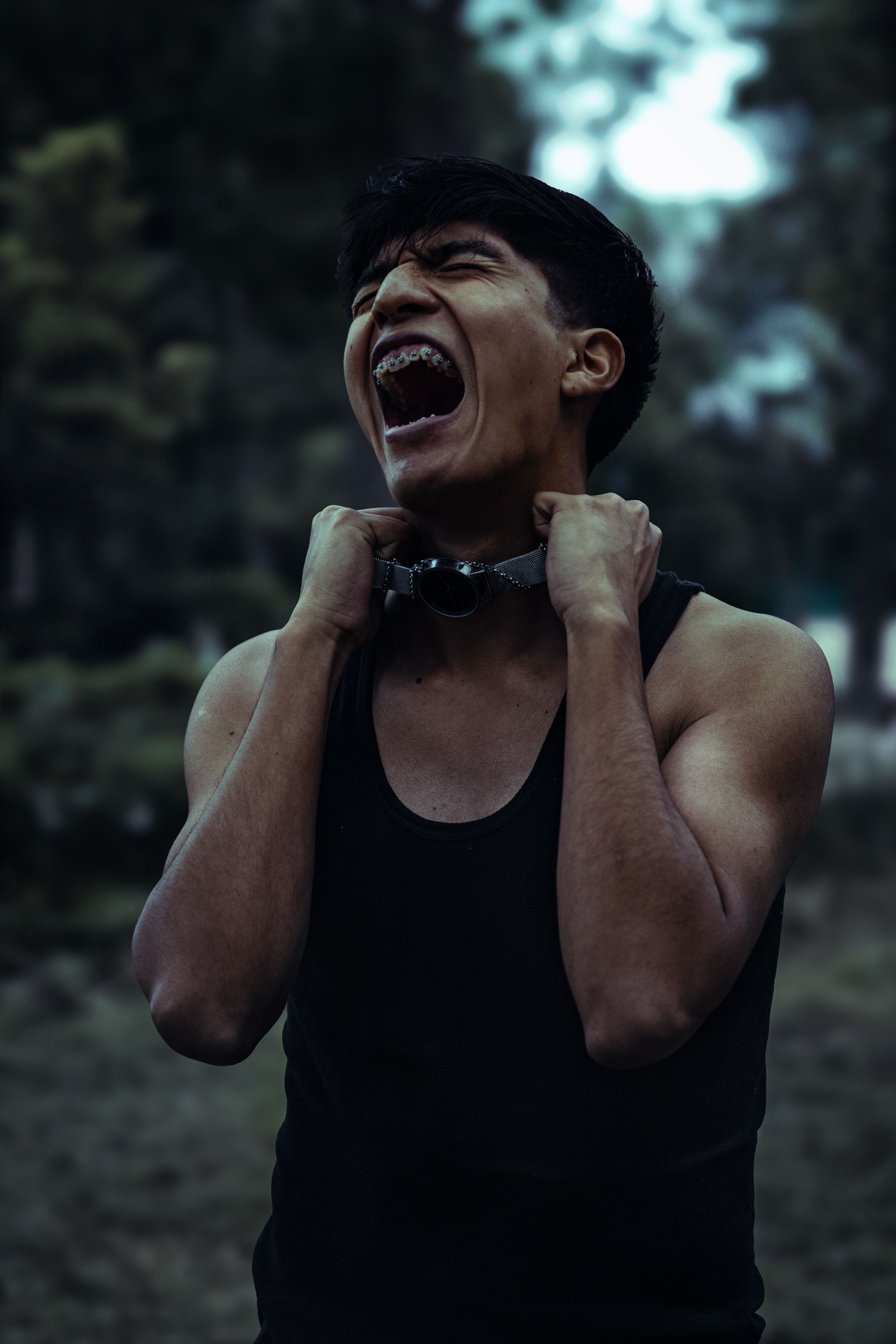 A powerful portrait of a young man outdoors expressing intense emotion, featuring a dark tone and moody atmosphere.