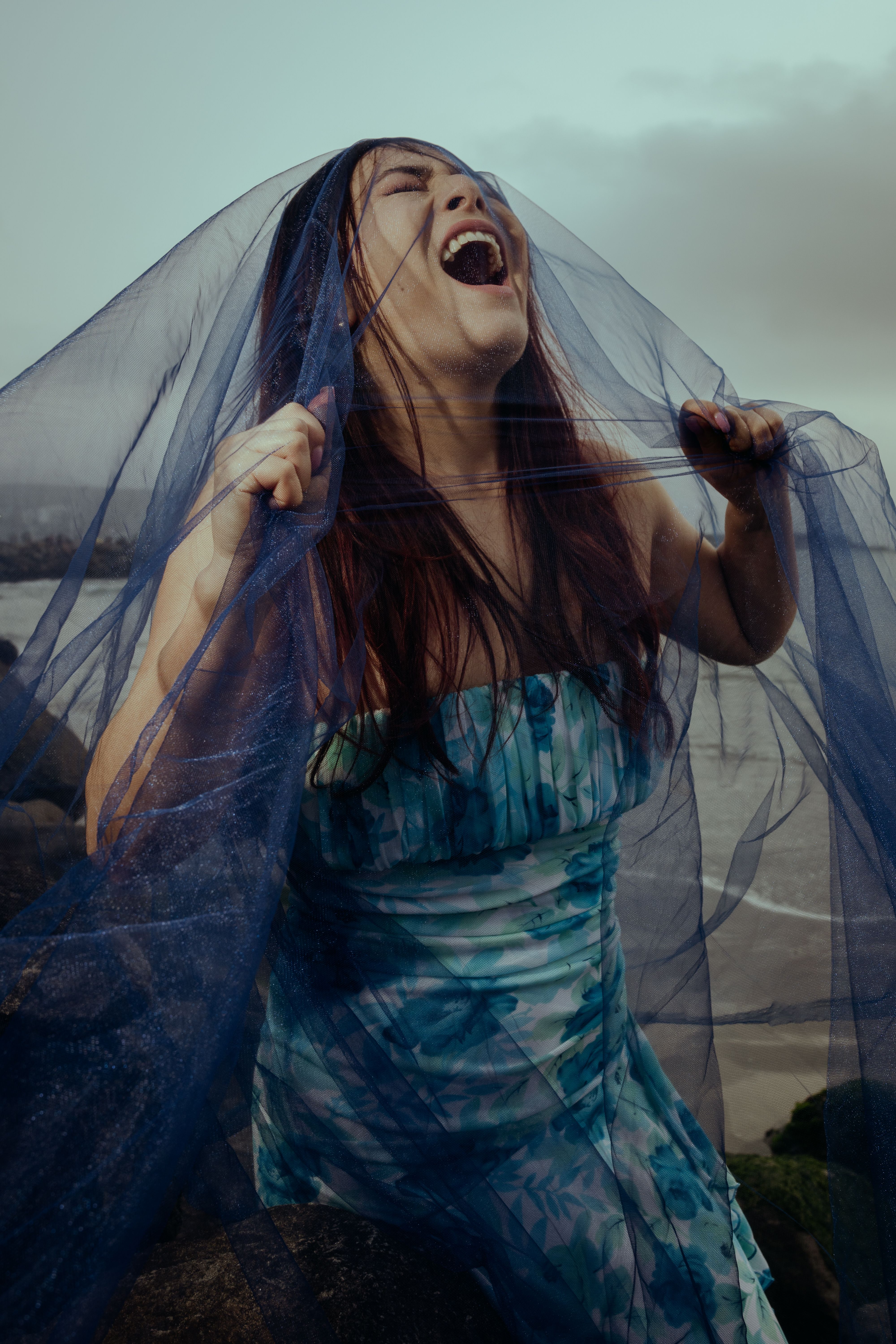 Captivating portrait of a young woman with a blue veil by the seaside in Lima, Peru, showcasing emotional expression.