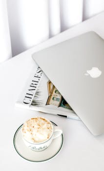 A sleek laptop beside a cappuccino on a bright, modern workspace.