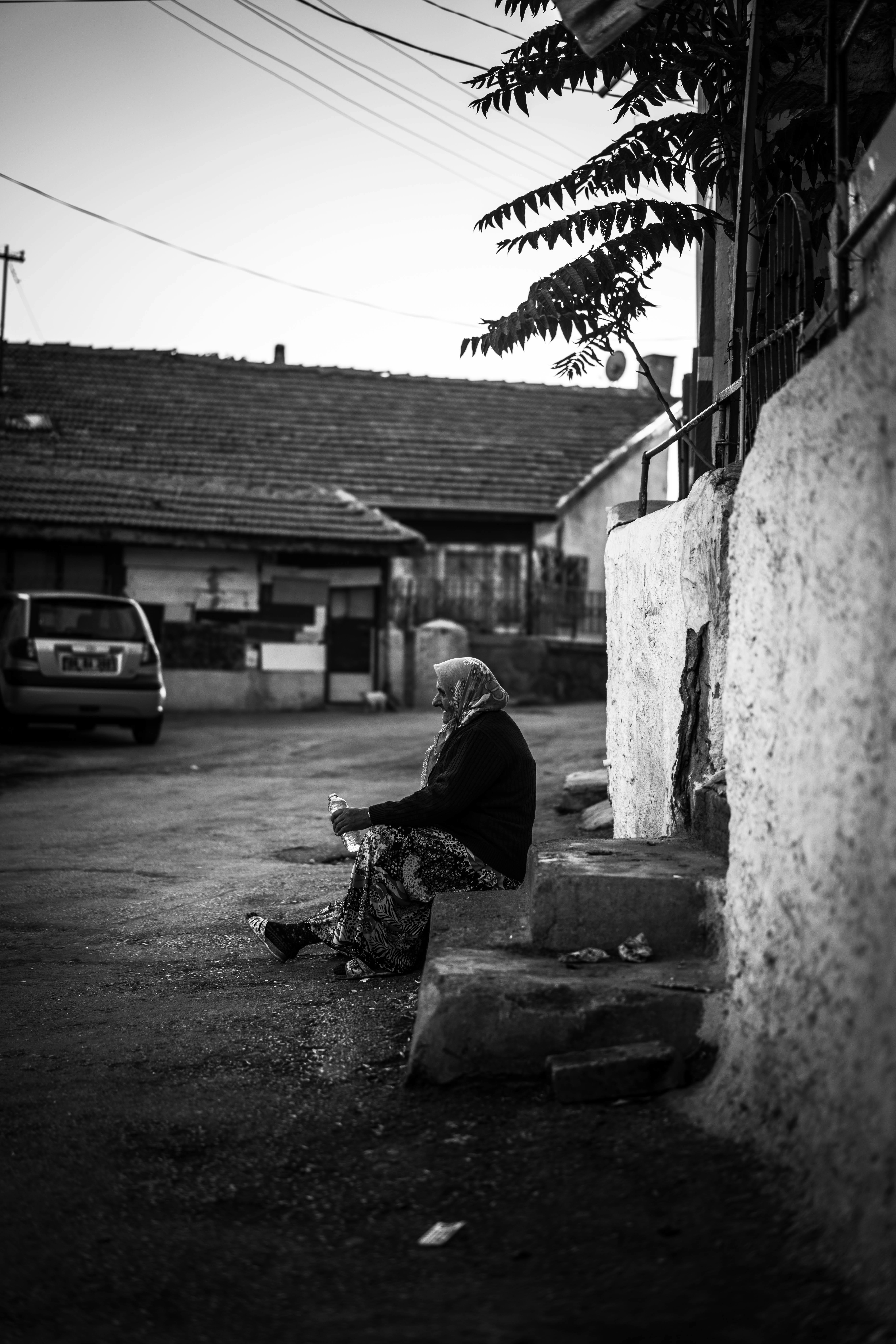 Black and white photo of an elderly woman sitting on village steps in Ankara, Türkiye.
