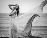 一位年轻女子身穿飘逸连衣裙，在海边的黑白肖像中散发出优雅的气质