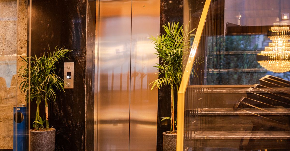 Elegant hotel elevator with lush plants and modern staircase, reflecting luxury and sophistication.