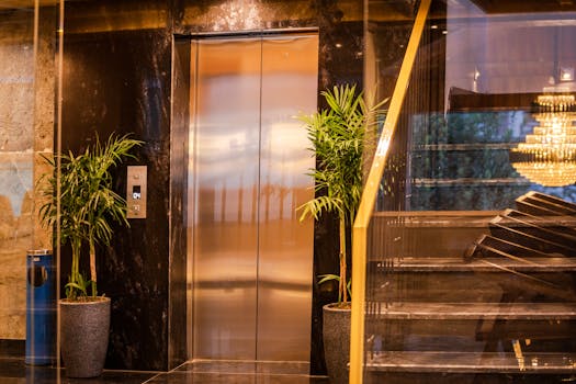 Elegant hotel elevator with lush plants and modern staircase, reflecting luxury and sophistication.