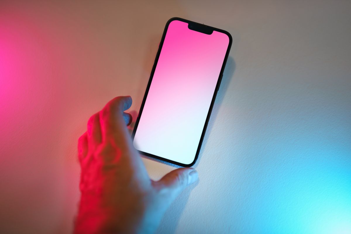 A hand reaching for a smartphone lying with its glowing gradient screen facing up
