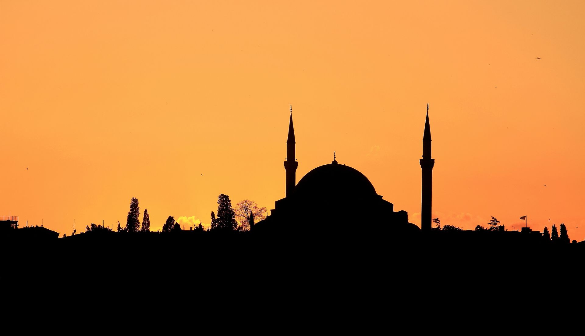 A striking silhouette of a mosque with minarets against a vivid sunset sky