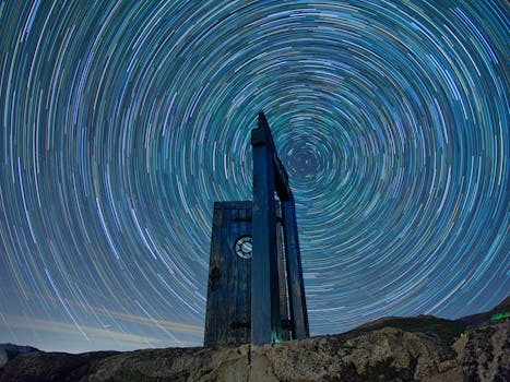 Dramatic star trail swirls over a mountain monument captured in a long exposure night sky.
