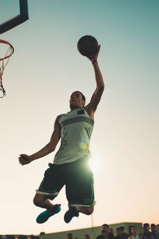 Basketball player performing a powerful dunk during sunset on an outdoor court.