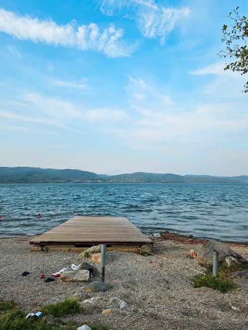 Free Tranquil lakeside scene with a wooden pier, distant hills, and clear blue sky. Stock Photo