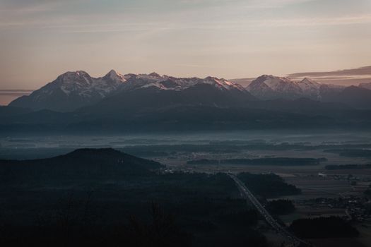 Serene view of snow-capped mountains at dusk with foggy valleys below, showcasing nature's tranquility.