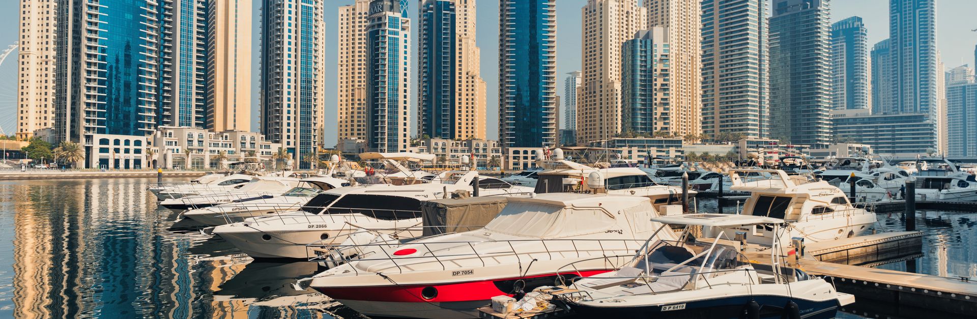 Scenic view of Dubai Marina's modern architecture and luxury yachts under blue sky.