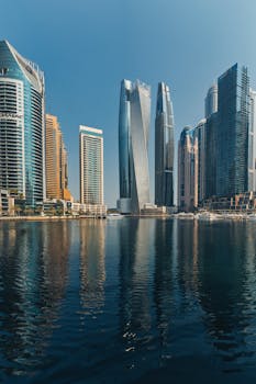 A striking view of Dubai Marina's skyscrapers reflecting in calm water under a clear blue sky.