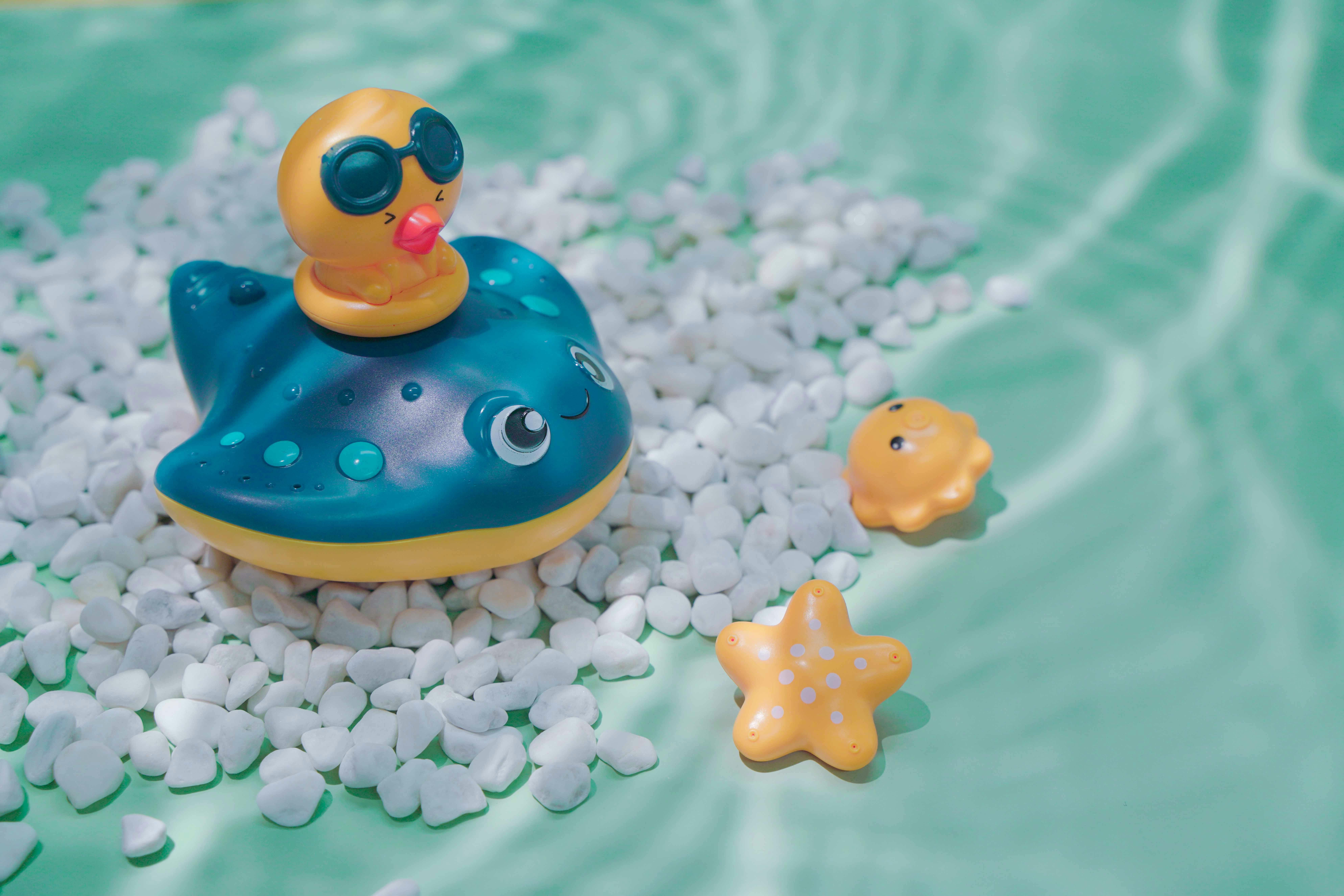 Cute rubber duck and starfish toys on white pebbles in a turquoise pool, perfect for summer fun.