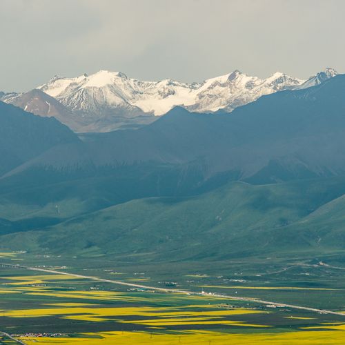 Free A breathtaking view of snow-capped mountains overlooking a lush green valley with yellow fields. Stock Photo